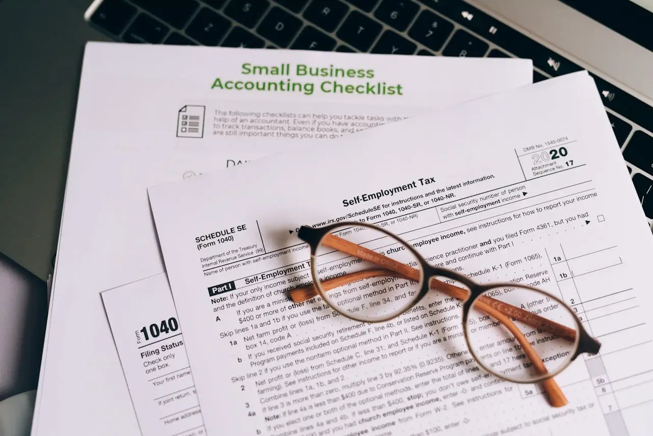 Close-up of tax forms and a small business accounting checklist on a laptop.